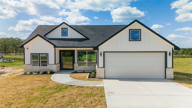 modern farmhouse with a garage, concrete driveway, a front lawn, and a shingled roof