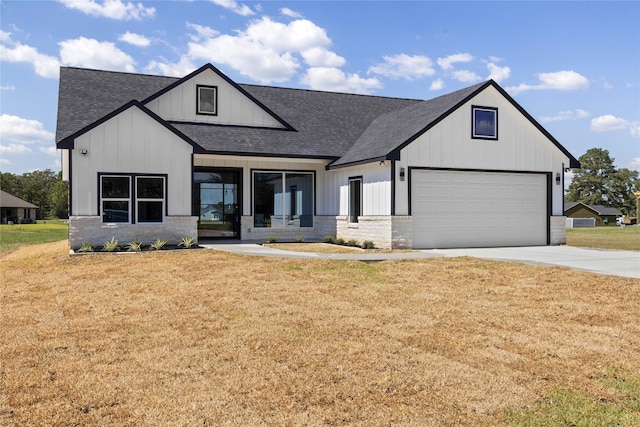 modern farmhouse style home with a garage, concrete driveway, a front lawn, and stone siding