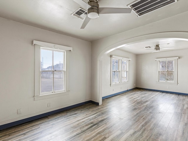 empty room with plenty of natural light, wood finished floors, and visible vents