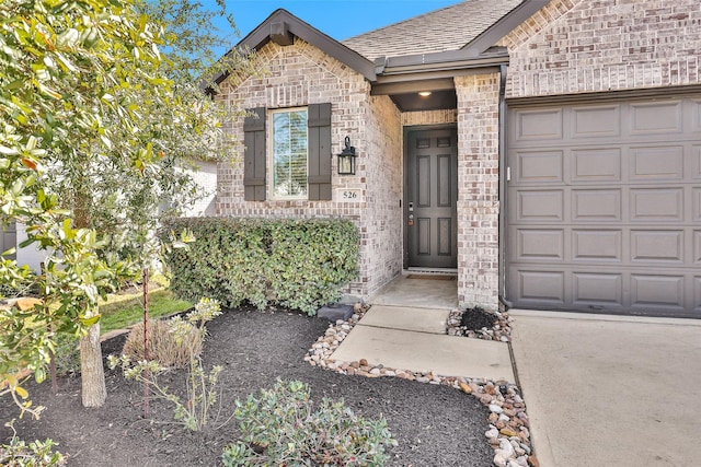 doorway to property with a shingled roof, brick siding, and an attached garage