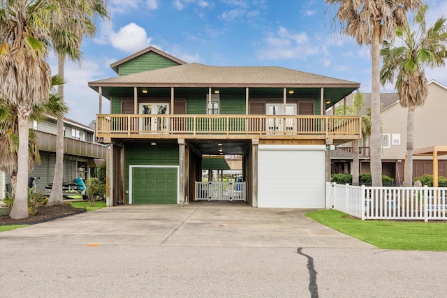 view of front of house featuring roof with shingles, an attached garage, fence, a carport, and driveway