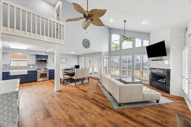 living area with light wood finished floors, a ceiling fan, a high ceiling, a fireplace, and recessed lighting