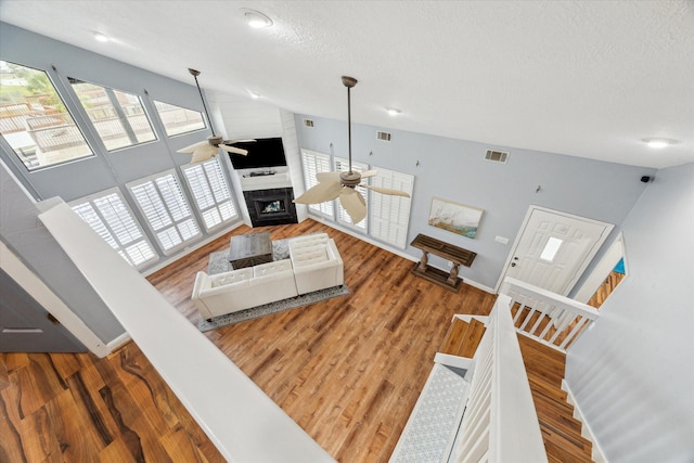 living room featuring visible vents, a ceiling fan, a large fireplace, a textured ceiling, and wood finished floors