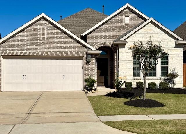 view of front of home featuring stone siding, an attached garage, concrete driveway, and a front yard