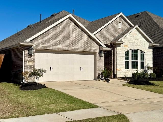 view of front of house featuring stone siding, brick siding, a garage, and driveway