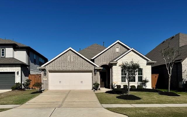 view of front facade with a front lawn, driveway, fence, a garage, and brick siding