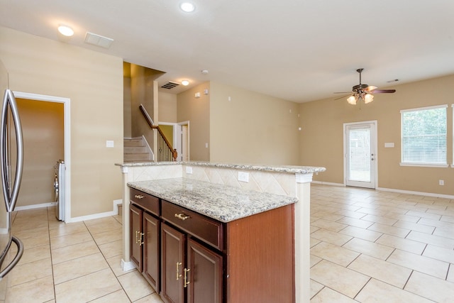 kitchen with tasteful backsplash, a center island, light tile patterned floors, ceiling fan, and light stone counters