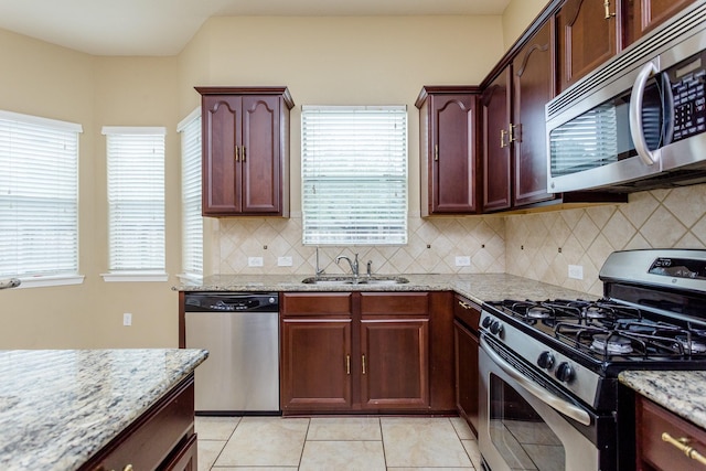 kitchen with sink, light tile patterned floors, stainless steel appliances, light stone countertops, and backsplash