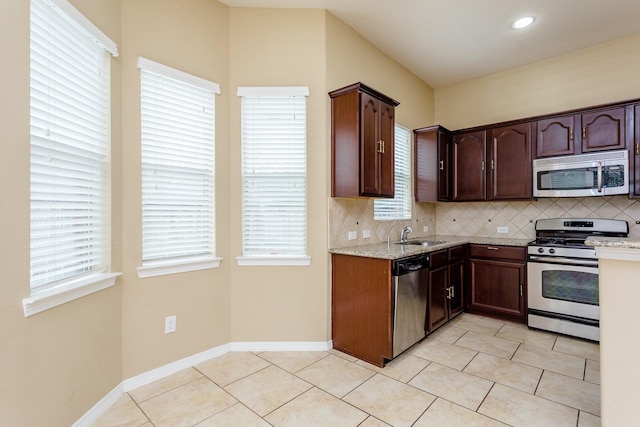 kitchen featuring light tile patterned floors, backsplash, stainless steel appliances, dark brown cabinetry, and light stone countertops