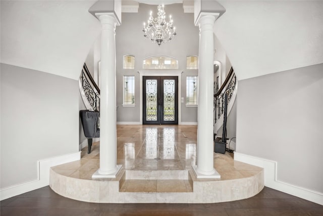 entrance foyer with ornate columns, hardwood / wood-style flooring, an inviting chandelier, and a towering ceiling