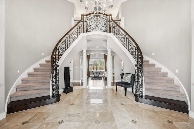 foyer entrance featuring a towering ceiling, a notable chandelier, and ornate columns