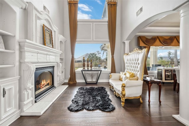 sitting room featuring dark wood-type flooring, a healthy amount of sunlight, decorative columns, and a high ceiling