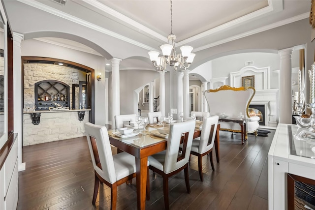 dining space featuring ornamental molding, a tray ceiling, dark hardwood / wood-style flooring, and decorative columns