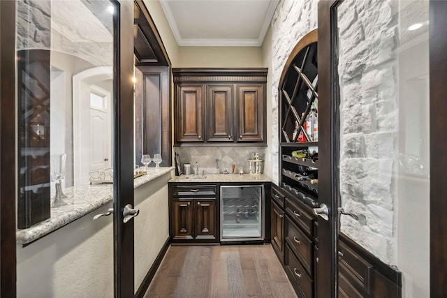 wine room featuring ornamental molding, dark wood-type flooring, bar, and wine cooler