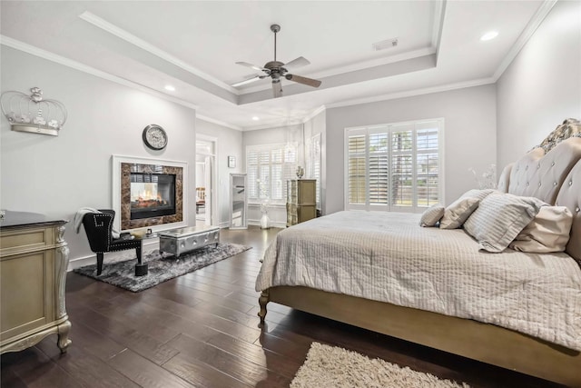 bedroom with crown molding, a premium fireplace, dark hardwood / wood-style floors, and a raised ceiling