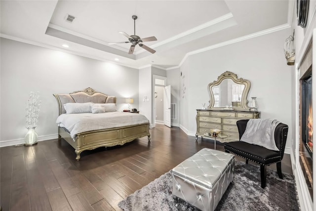 bedroom featuring dark hardwood / wood-style flooring, a tray ceiling, ornamental molding, and ceiling fan