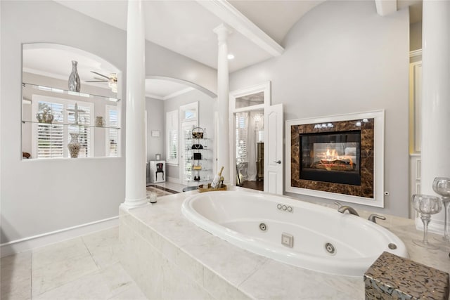 bathroom with tiled tub, a high end fireplace, decorative columns, and ceiling fan