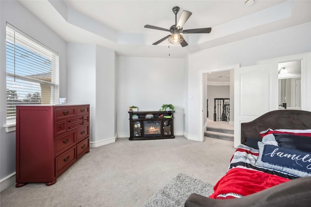 bedroom with ceiling fan, light colored carpet, and a tray ceiling