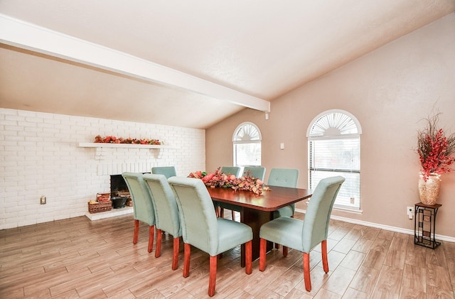 dining room with a fireplace, vaulted ceiling with beams, light hardwood / wood-style floors, and brick wall