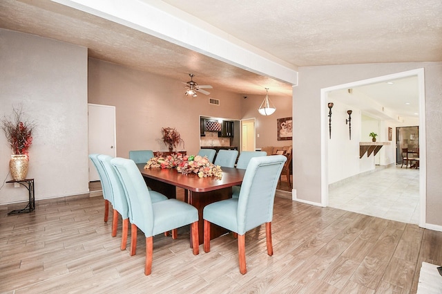 dining area featuring ceiling fan, light wood-type flooring, vaulted ceiling, and a textured ceiling