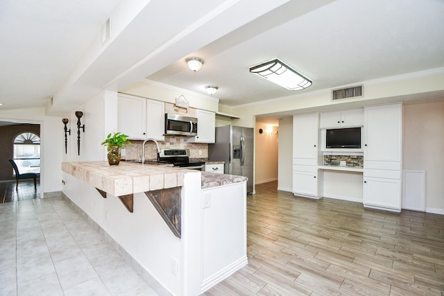 kitchen featuring appliances with stainless steel finishes, white cabinetry, light hardwood / wood-style floors, kitchen peninsula, and tasteful backsplash