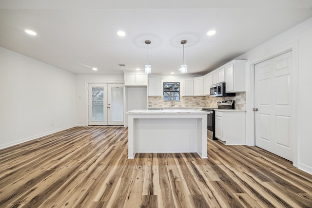 kitchen featuring appliances with stainless steel finishes, pendant lighting, white cabinetry, backsplash, and light hardwood / wood-style floors