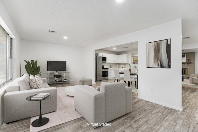 living area with a textured ceiling, light wood-style flooring, recessed lighting, visible vents, and baseboards