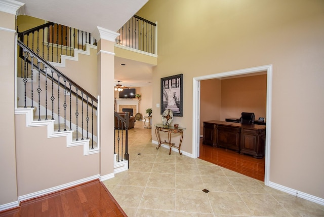 entrance foyer with a fireplace, light tile patterned floors, a towering ceiling, a ceiling fan, and baseboards