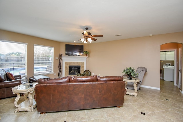 living room featuring light tile patterned floors, arched walkways, baseboards, ceiling fan, and a fireplace