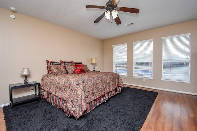 bedroom with a ceiling fan, wood finished floors, visible vents, and baseboards