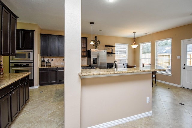 kitchen with pendant lighting, light tile patterned floors, stainless steel appliances, decorative backsplash, and light stone countertops