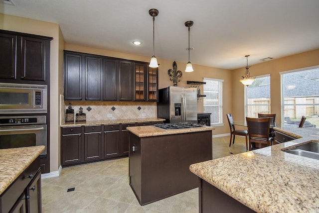 kitchen with dark brown cabinetry, appliances with stainless steel finishes, a center island, glass insert cabinets, and pendant lighting