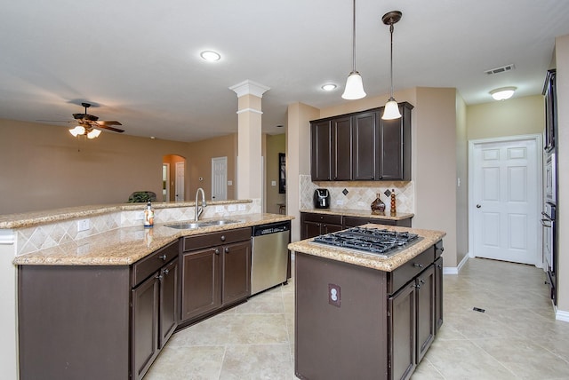 kitchen with a kitchen island with sink, stainless steel appliances, a sink, dark brown cabinets, and decorative light fixtures