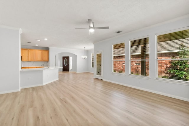 unfurnished living room with ceiling fan with notable chandelier, light hardwood / wood-style floors, sink, and crown molding