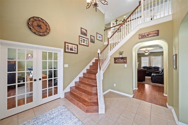 tiled entrance foyer with a high ceiling, a notable chandelier, and french doors