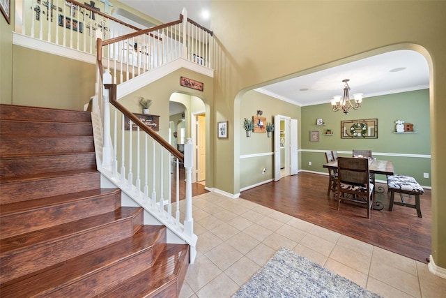 tiled entryway with a notable chandelier, ornamental molding, and a high ceiling