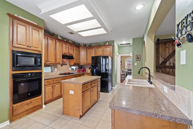 kitchen featuring sink, a kitchen island, a barn door, decorative backsplash, and black appliances