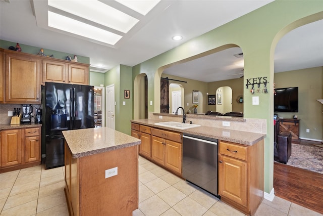 kitchen featuring sink, a kitchen island, light stone counters, black fridge, and stainless steel dishwasher