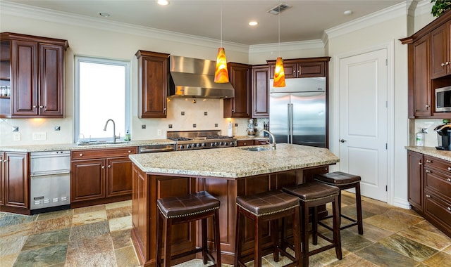 kitchen with wall chimney exhaust hood, stainless steel appliances, sink, and a center island with sink