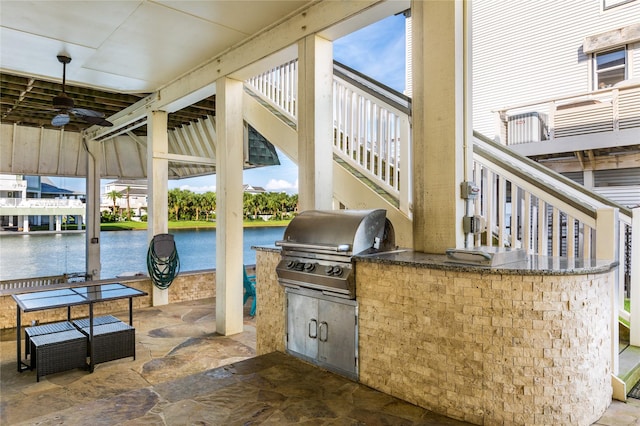 view of patio featuring area for grilling, a water view, ceiling fan, and exterior kitchen