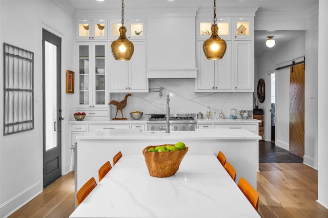 kitchen featuring hanging light fixtures, white cabinets, a barn door, light stone countertops, and backsplash