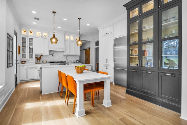 kitchen featuring crown molding, built in refrigerator, pendant lighting, a kitchen island with sink, and backsplash