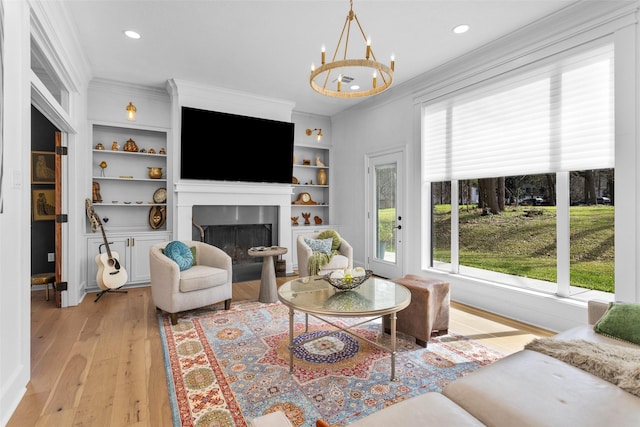 living room featuring crown molding, an inviting chandelier, light hardwood / wood-style floors, and built in shelves