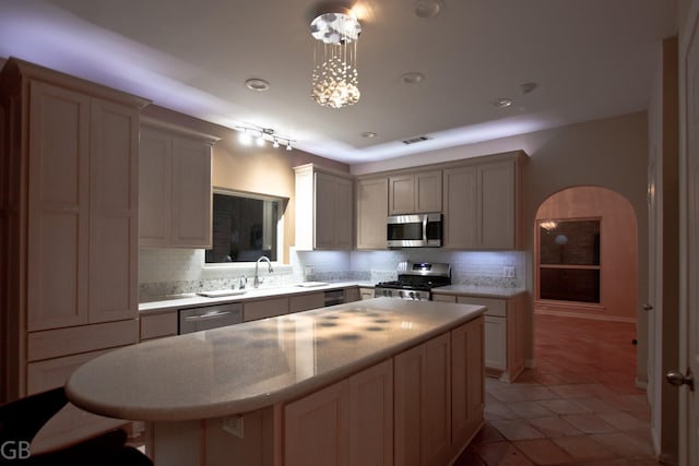 kitchen with appliances with stainless steel finishes, sink, backsplash, a center island, and decorative light fixtures