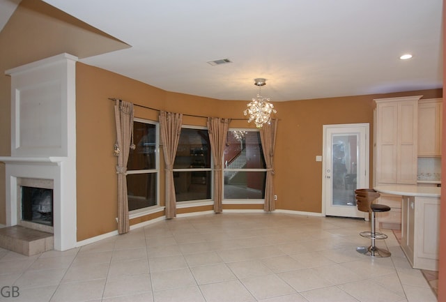 unfurnished dining area featuring a tiled fireplace, an inviting chandelier, and light tile patterned floors