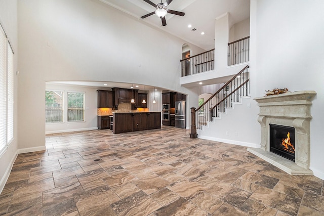 unfurnished living room with a high ceiling, ceiling fan, and a high end fireplace