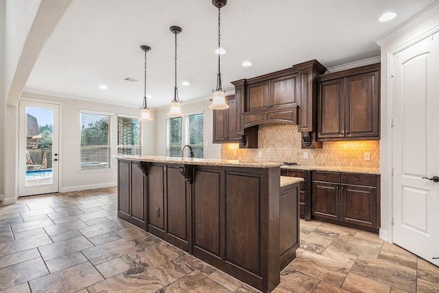 kitchen with a breakfast bar, hanging light fixtures, dark brown cabinets, and a center island with sink