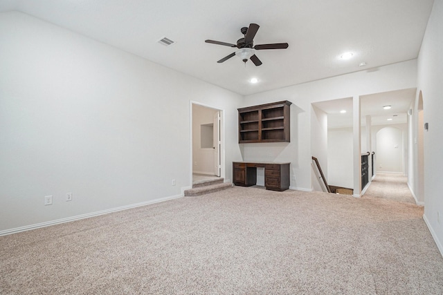 unfurnished living room with ceiling fan, light colored carpet, and built in desk