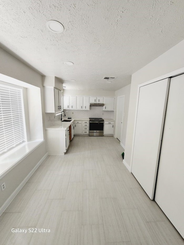 kitchen featuring white cabinetry, sink, decorative backsplash, stainless steel range oven, and a textured ceiling