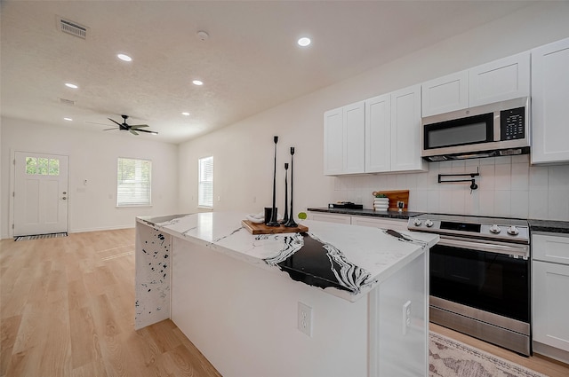 kitchen with light stone counters, stainless steel appliances, a center island, and white cabinets